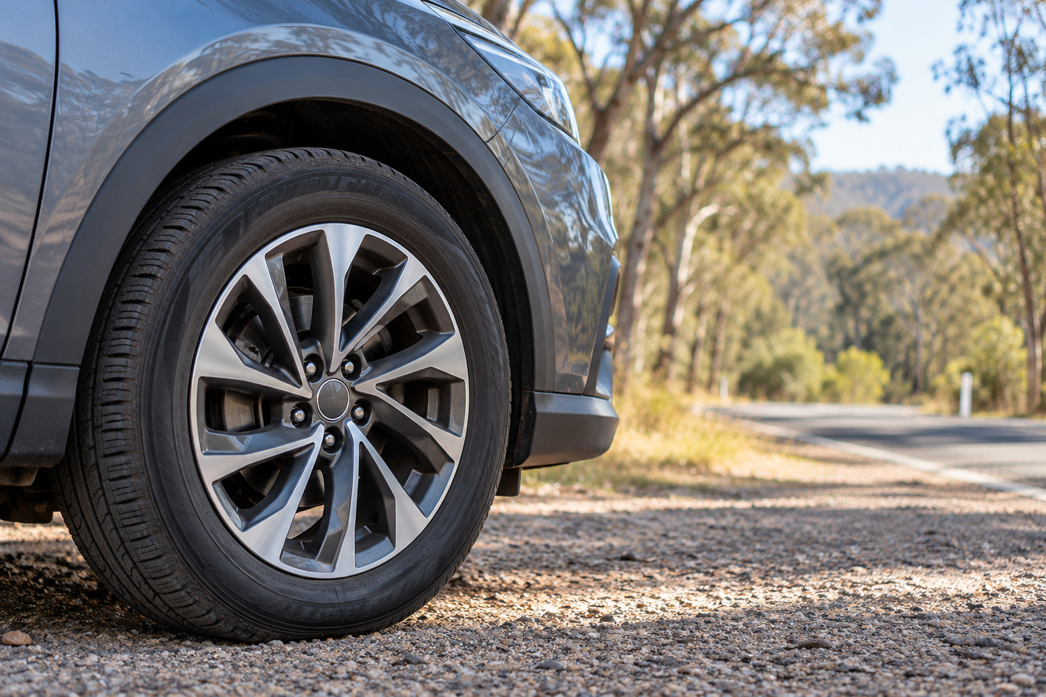 Front wheel of a modern car parked beside a quiet eucalyptus-lined road.